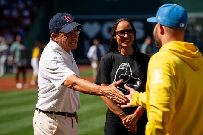 Tom Werner and Bekah Salwasser standing on the field shaking hands with Danny Coulombe who was walking onto the field. 
