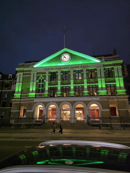 Tower Hamlets Town Hall illuminated in green at night, with a clock in the pediment.