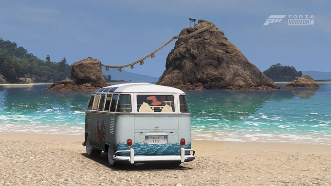 Una furgoneta vintage está estacionada en una playa de arena, orientada hacia el océano. En el fondo, hay una formación rocosa con un puente de madera que conecta dos partes. La imagen proviene del juego Forza Horizon 4.