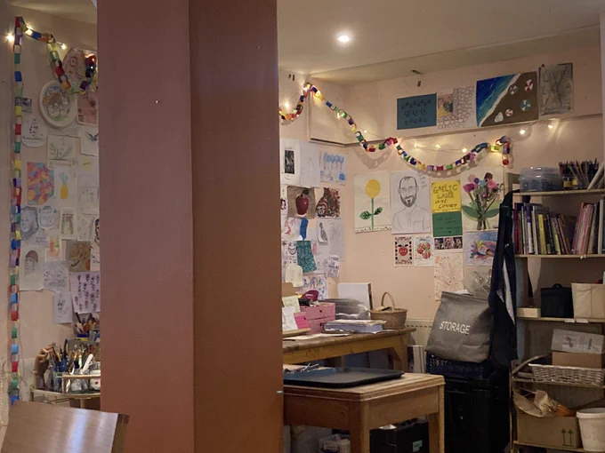 A fairy lit corner of the cafe with art stuff on a wooden table and pictures in the wall