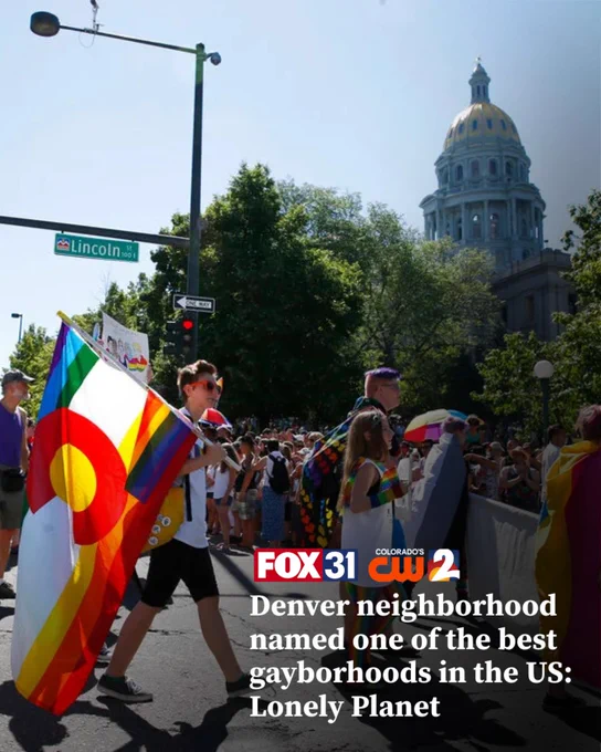 Crowd marches with rainbow and Colorado state pride flags near Denver's Capitol building during a pride event.