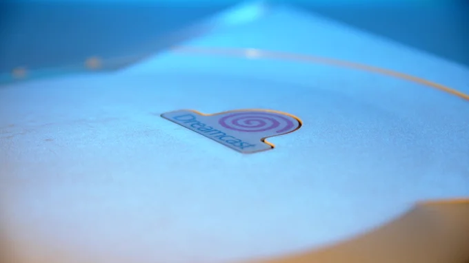 Close-up of the Dreamcast logo swirl on top of a Dreamcast video game console, lit in blue and orange lighting.