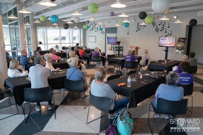 A full room of people watching a live stream on tv screens