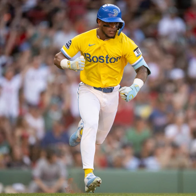 Ceddanne Rafaela running down the first base line wearing his yellow and blue City Connect jersey. 