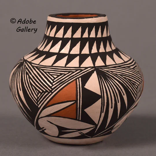 The body is highly decorated with intricate black fine-line elements, resembling yucca leaves and triangles. This fine-line work transitions into a secondary motif: black-outlined red triangles flanked by black and white adjacent triangles. A final, elegant touch is a long curve beneath the main design that terminates in a stylized bird's head.