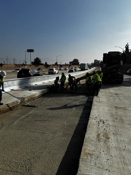 Workers pouring lean concrete base for new freeway lane. 