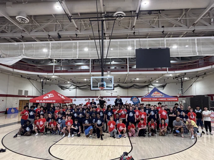 A large group gathers in a gymnasium setting, wearing matching sports attire. The mood is communal and energetic.