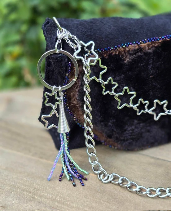 handbag made of black leather and natural seal skin, with glass aurora borealis shade beads, removable silvertone charms and chains, background of green grass and rose bush, closeup of charms 