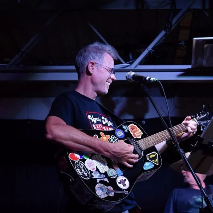 A person plays an acoustic guitar on a stage with dark lighting. 