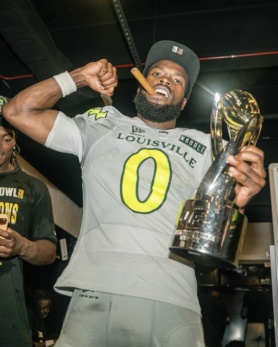 A joyful athlete in a 'LOUISVILLE' jersey celebrates winning a trophy. He is holding the trophy in one hand and a cigar in his mouth while cheering.
