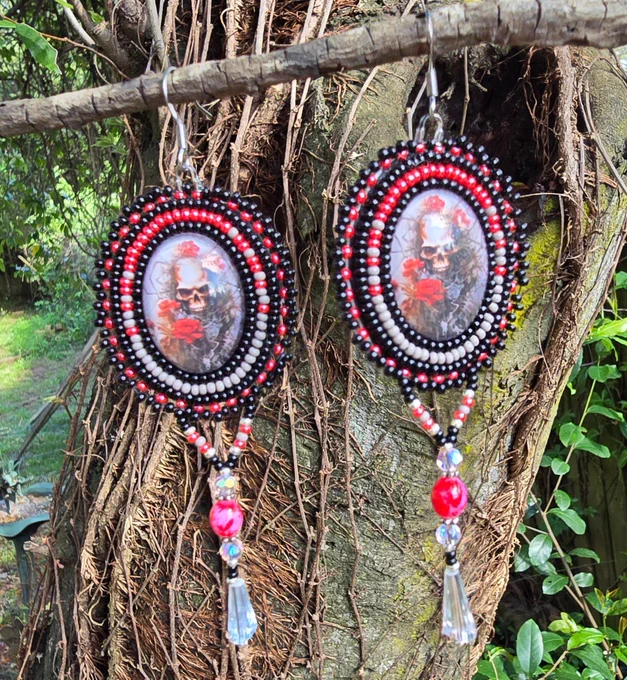 oval shaped beaded earrings, centers have graphics of skulls and reddish roses, surrounded by glass beads in shades of blacks, reds, and gray, stainless steel ear hooks 