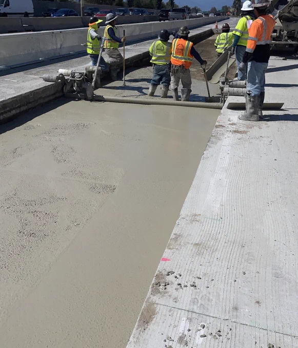 Workers pouring and leveling lean concrete base. 