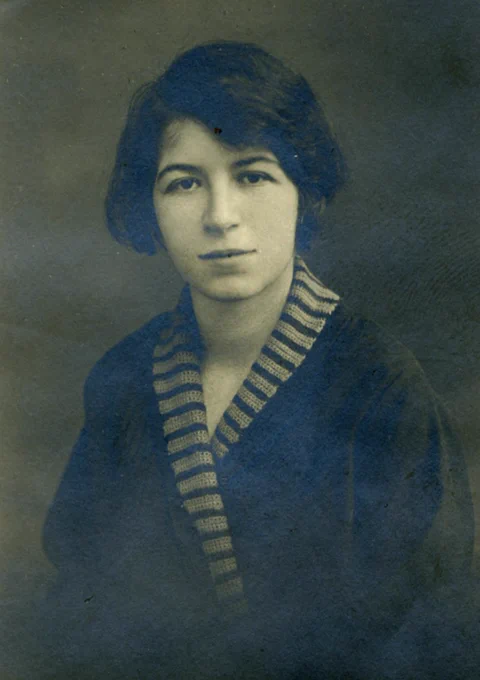 A portrait of a young woman with short hair, wearing a dark V-neck sweater with light stripes. 

