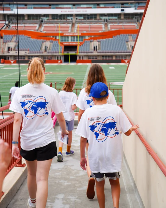 People in white shirts walk down a ramp into DKR Stadium. 