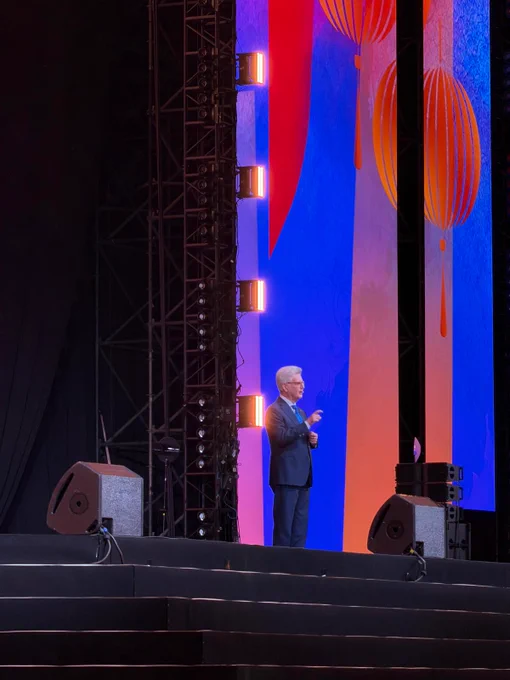Rotary International President Francesco Arezzo speaks on stage during the Opening General Session at #Rotary26. Bright lantern-themed graphics in pink, blue, and orange illuminate the backdrop behind him.