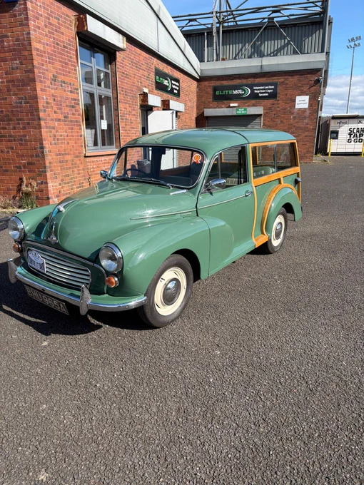 A classic green car with wood paneling is parked outside a brick building in clear weather. The scene has a nostalgic and charming mood.