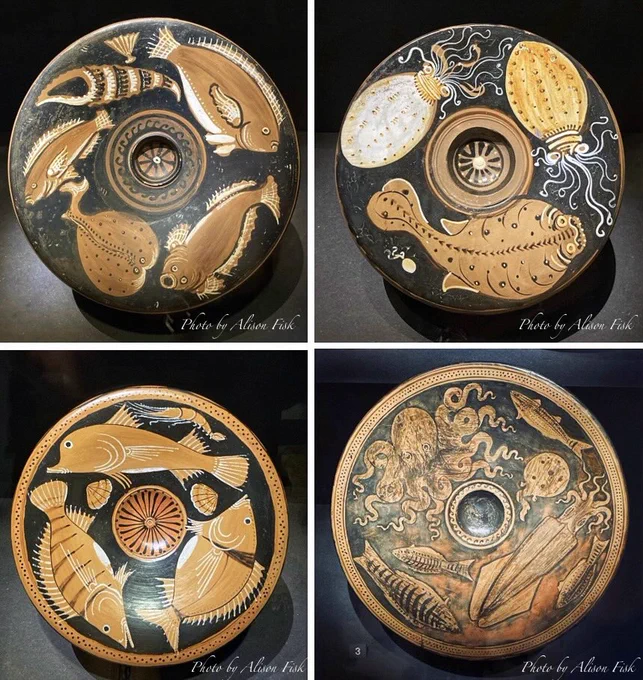 My photo collage shows four ancient Greek ‘Red-Figure’ ceramic fish plates arranged in a 2×2 grid. Each plate is circular with a black glazed background decorated in red with depictions of sea creatures. This gives the impression of looking into an underwater world. Each plate has a circular central depression, perhaps a well used for oil or sauce.