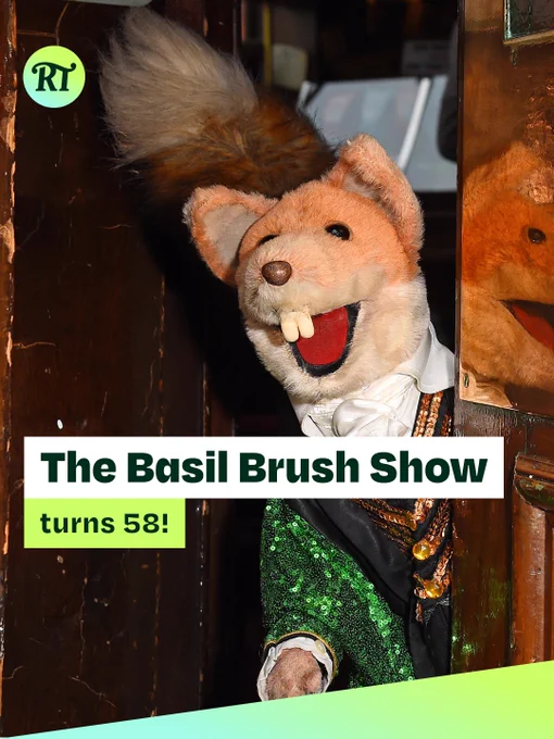 Promotional graphic featuring Basil Brush, the famous fox puppet, peeking around a doorway with a wide smile. He wears a green sequinned jacket, white cravat and decorative gold chains. An RT logo appears in the top-left corner. Overlaid text reads: “The Basil Brush Show turns 58!” A green gradient banner runs diagonally across the bottom of the image.
