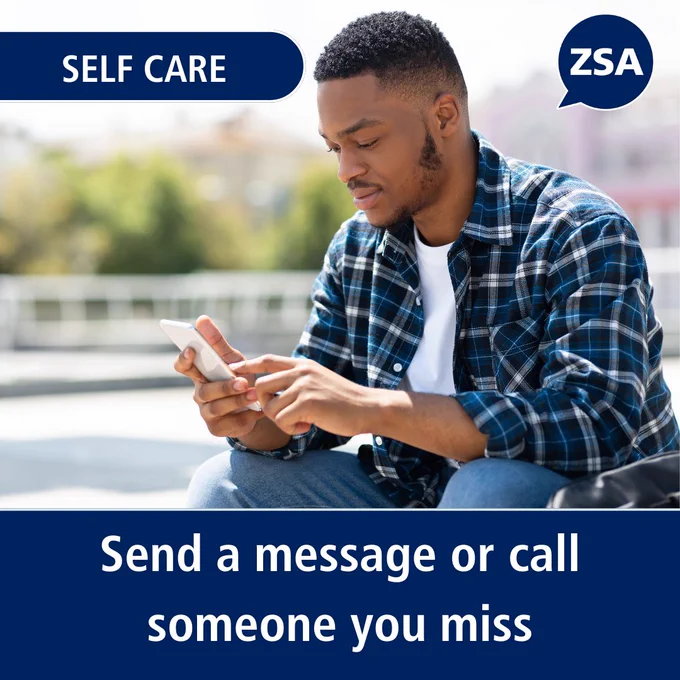 Young man in a plaid shirt sitting outdoors, using his phone to reach out to someone he misses.