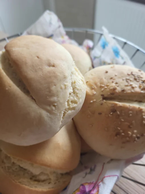Selbstgebackene Sonntagsbrötchen, mit und ohne Sesam. 
Sie sind in einem Drahtkörbchen mit einer Schmetterlingsservierte.  