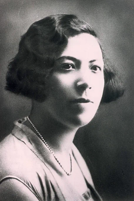 Black and white portrait of a woman with short curly hair, wearing a light-colored outfit and a delicate necklace.