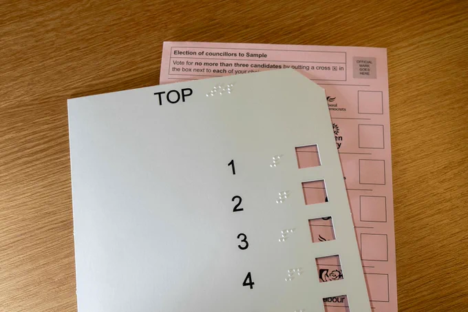 A sample election ballot paper with a Braille overlay card for visually impaired voters.