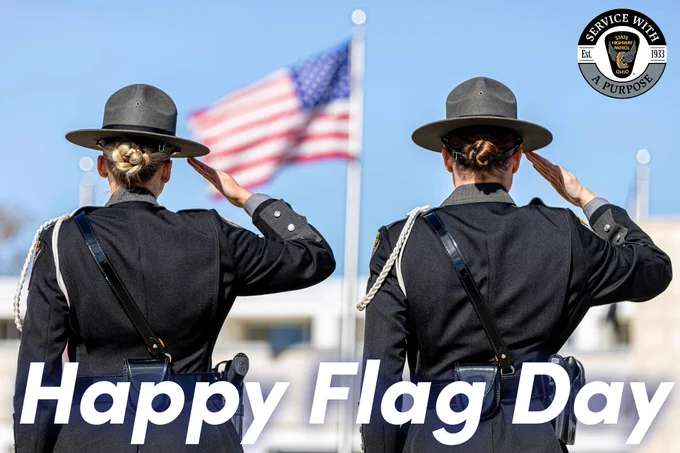 The back of two female troopers saluting the American flag with the words, "Happy Flag Day."