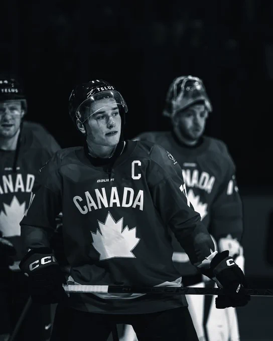 Black and white picture of Macklin Celebrini with the C on his team Canada jersey 