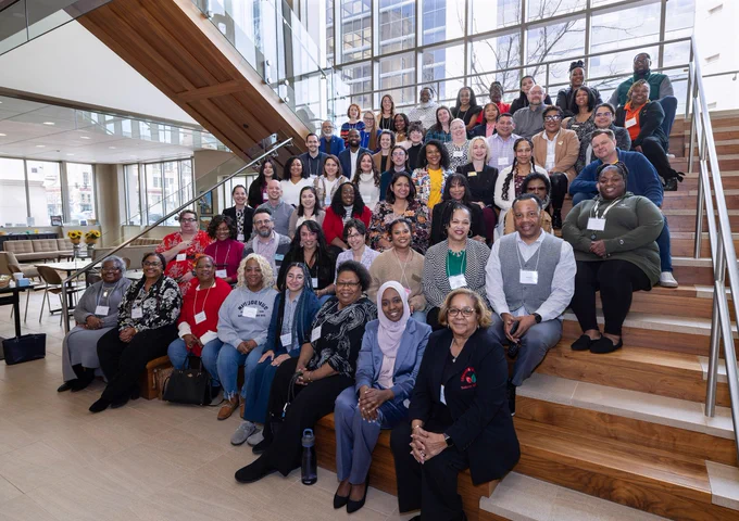 A large group of people poses for a photo on a staircase and landing in a modern building with large windows and natural light.