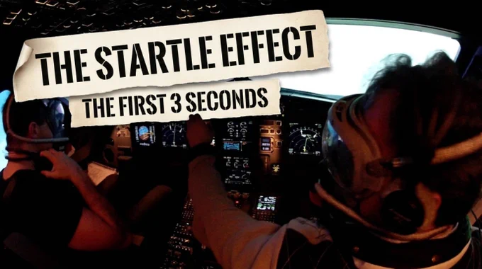 A wide fish-eye view of an Airbus flight deck in bright daylight, two pilots in oxygen masks, one reaching forward across the centre console toward the panel in a busy hands-on moment. Two torn-paper magazine-cutout ribbons in bold black stencil capitals overlay the photo: a top ribbon reading 'THE STARTLE EFFECT' and a lower ribbon reading 'THE FIRST 3 SECONDS.'