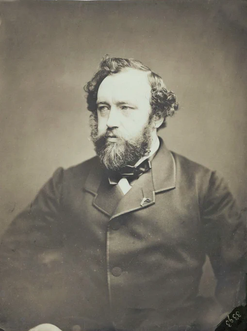 Retrato de Adolphe Sax, un hombro con amplias entradas y pelo algo rizado y gran barba con bigote perfilado, elegantemente vestido con levita cerrada y posando en actitud orgullosa. Dominio público.