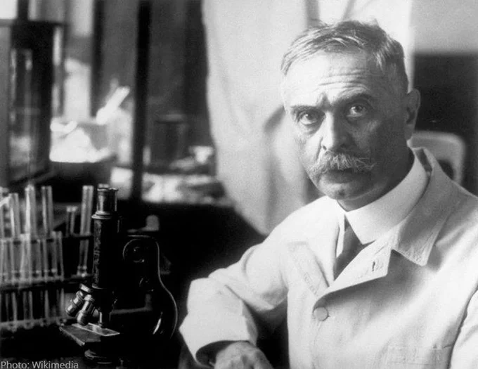 Karl Landsteiner sitting in a laboratory next to a microscope.