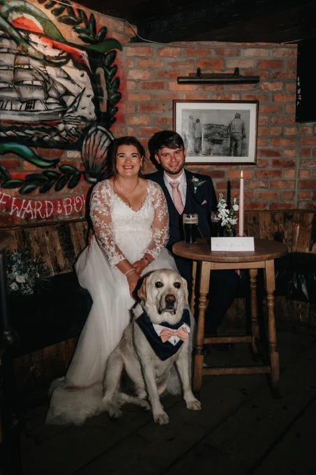 A couple pose on their wedding day with a large breed dog sitting in front on them.