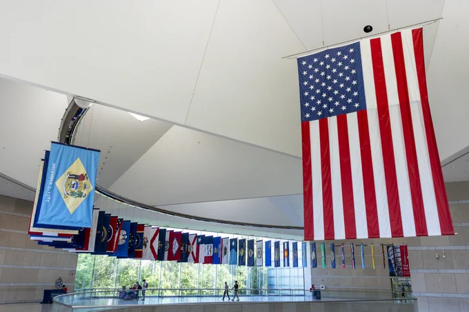 Large American flag hanging prominently inside a modern building with a curved ceiling and multiple state flags displayed along the wall.