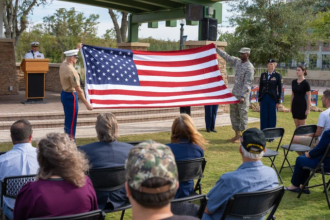 a photo of members of the military holding an american flag in from of the veterans pavilion on campus