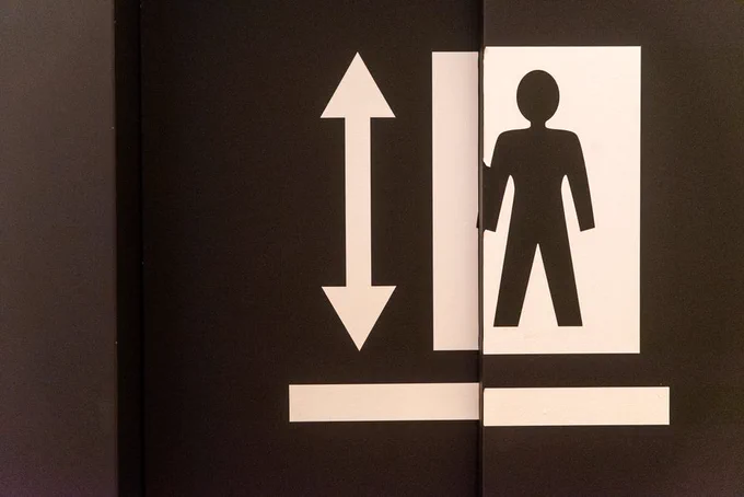 Graphic of an elevator door with a human figure and directional arrow symbol.
