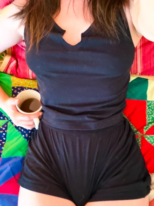 a top down view of a brunette lying in bed, coffee in hand