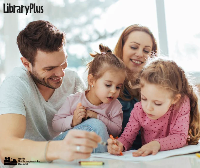 A family of four engaged in drawing and colouring together at a bright table near a large window.