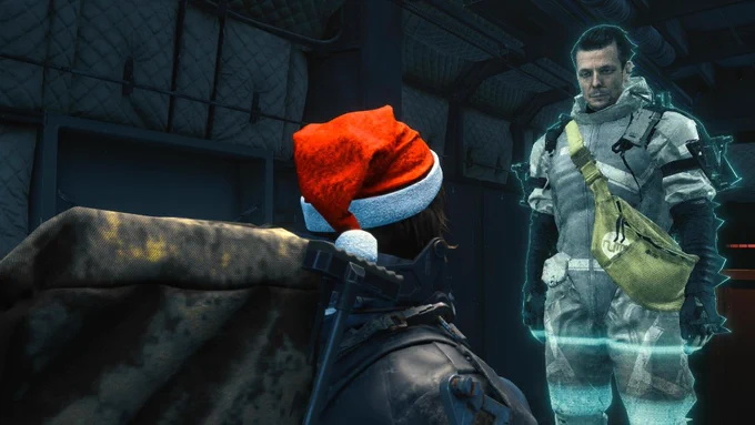 Sam aus Death Stranding Directors Cut trägt eine rote Weihnachtsmütze. Er steht in einem dunklen Raum und schaut auf das blau leuchtende Hologramm eines anderen Porters.