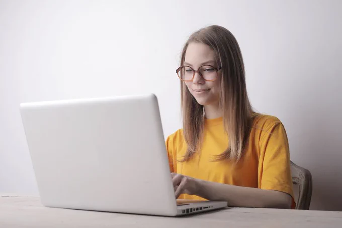 Smiling woman in glasses working on a laptop indoors, focused on screen.