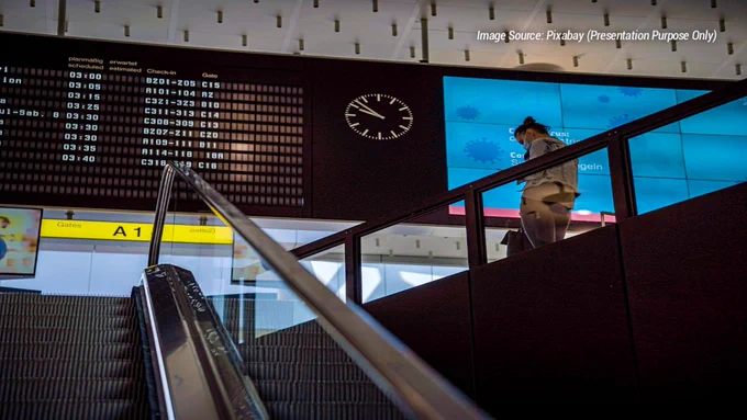 Traveler at an airport terminal using a mobile device to compare flight prices and search for airfare deals. The image represents modern AI flight search tools that help travelers track fare changes, compare travel dates, discover cheaper routes, and monitor airfare trends before booking. Airport departure screens, travel planning, and digital booking technology highlight how platforms such as Google Flights, Hopper, Skyscanner, Kayak, and Momondo assist with finding lower airfares. The scene reflects smarter travel planning, fare alerts, flight comparison research, budget travel strategies, and the growing use of AI-powered tools for booking flights in 2026.