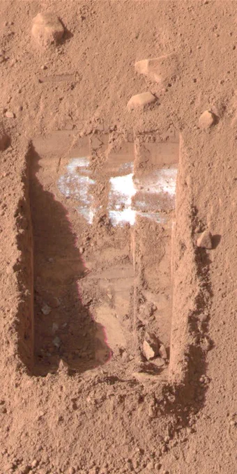 NASA's Phoenix Mars Lander's robotic arm scooped up loose orangey soil to create a shallow trench. White dice-sized chunks were revealed, as seen in the upper right-hand portion of this image.