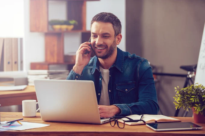 man sat in front of laptop whilst using mobile phone