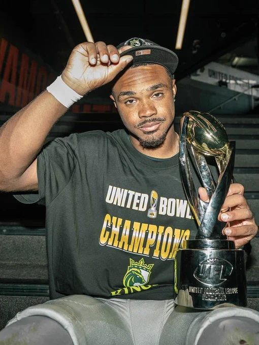 A victorious athlete wearing a United Bowl Champions shirt holds a trophy with pride, exuding confidence and joy after a major win.