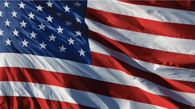 Close-up of the United States flag waving in the wind, with its blue field of white stars and red-and-white stripes filling the image.