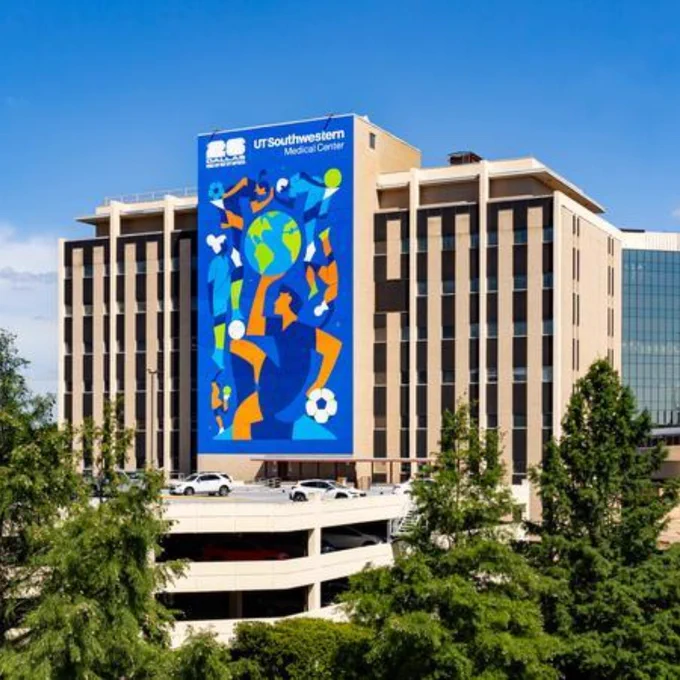 UT Southwestern Medical Center building with a large colorful mural featuring abstract human figures, a globe, and soccer balls on its facade.