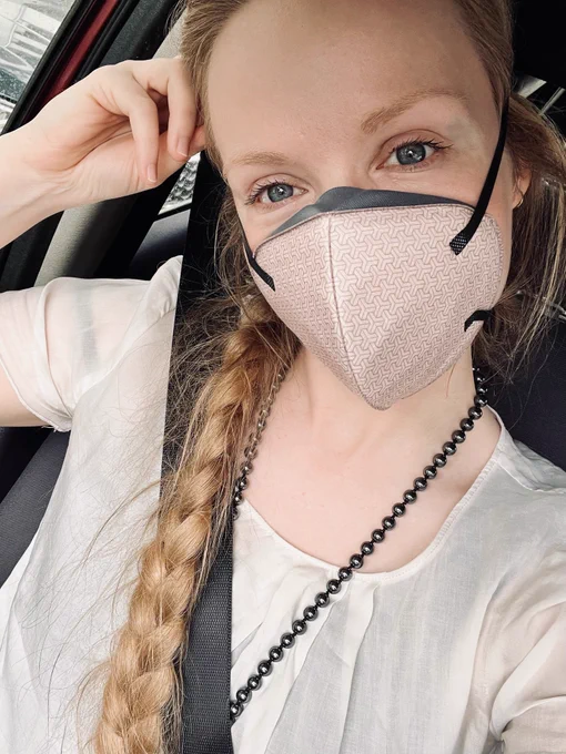 Thirst Masker in a car, wearing a white shirt & a metallic pearl necklace.