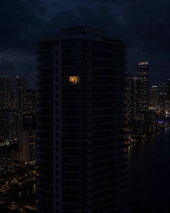 A brightly lit window stands out on a dark building, with a skyline filled with lights reflecting city life at night.