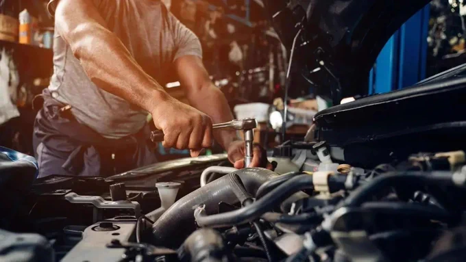 Ein Mechaniker konzentriert sich auf die Reparatur eines Autos in einer Werkstatt, wobei warme Lichtstrahlen eine geschäftige Atmosphäre erzeugen.

Die Bildkomposition fokussiert sich eng auf die Hände des Mechanikers, die mit einem Werkzeug am offenen Motor eines Autos arbeiten. Der Ausschnitt und die Nahaufnahme betonen die Präzision und den technischen Aspekt der Tätigkeit. Die Elemente sind so angeordnet, dass der Blick des Betrachters sofort auf die Arbeitshandlungen gelenkt wird. Der Mechaniker ist von vorne leicht angeschnitten, und die Hauptaktion, das Drehen mit dem Schraubenschlüssel, füllt den zentralen Teil des Bildes aus.