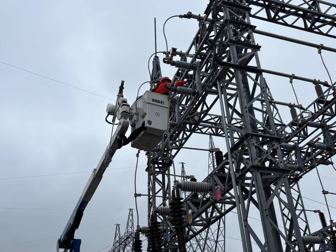 A powerline technician in a bucket truck works on an electrical structure 